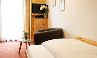 A cozy hotel room with a single bed and an armchair. The room is bright and inviting, featuring a table and a television.