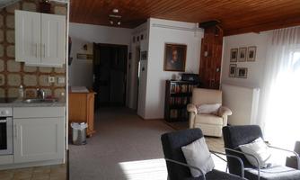 A cozy living room with a kitchenette and a bright decor. The room is well-lit and displays a warm atmosphere.