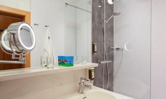 A modern bathroom with a shower and a sink. On the shelf, there is a mirror and a small colorful object.
