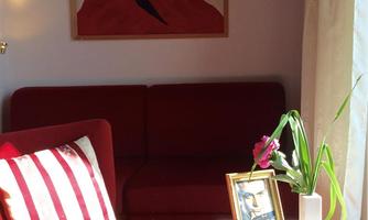 A cozy room with a red sofa and a table. On the wall hangs a picture of a woman with red hair.