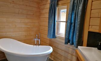 A modern bathroom with a freestanding bathtub and a sink. The walls are made of wood, and the curtains are blue.