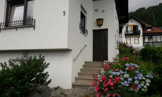 A stylish house with a staircase and colorful flowers in the foreground. The facade is bright and inviting.