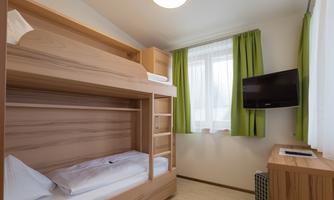 A simple bedroom with a wooden bunk bed. The walls are light, and there are green curtains as well as a television on the wall.