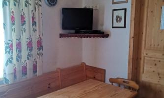 A cozy dining area with a wooden table and chairs. A TV and decorative pictures hang on the wall.