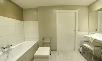 A modern bathroom with a bathtub, a large mirror, and bright tiles. It is well-lit and looks clean and inviting.