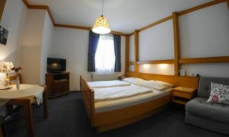 A quiet hotel room with two beds, a table, and a sofa. There is a television and a window with curtains.