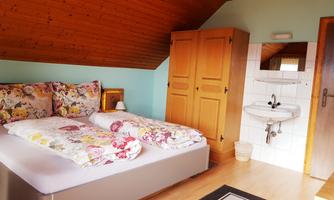A cozy bedroom with two beds and colorful pillows. There is a wooden wardrobe and a small sink in the room.