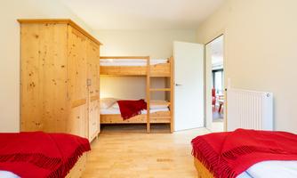 A simple bedroom with a loft bed and two single beds. There is a built-in wardrobe and bright walls.
