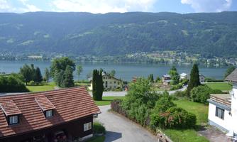 A picturesque landscape with a tranquil lake and gentle hills in the background. In the foreground, there are some houses and green grass visible.