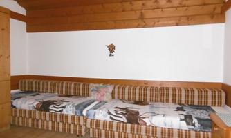 A cozy room with a long bench and wooden paneling. The bench is upholstered with checkered fabric and has blankets with animal motifs.