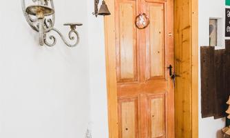 An inviting wooden front door with a welcome sign. To the left, there is a decorative wall lamp and a small flower arrangement.