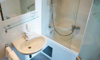 A modern bathroom with a sink and a shower. The walls are tiled in light colors and there is a mirror above the sink.