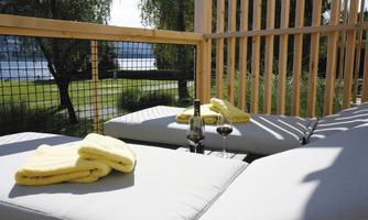A cozy lounging area with yellow towels and a glass of red wine. In the background, there is a beautiful view of water and trees.
