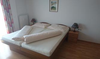 A cozy bedroom with a large double bed and two nightstands. The room has bright walls and a wooden floor.