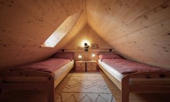 A cozy bedroom in the attic with two single beds. The room has wooden paneling and a small nightstand.