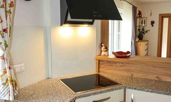 A modern kitchen with bright cabinets and a granite countertop. Above the cooktop hangs a black range hood.