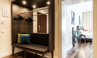 A modern entrance area with a wardrobe and a bench. In the background, a room with a bed and a bicycle is visible.
