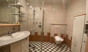 A modern bathroom with a transparent shower and a large sink. The floor is designed in a black and white checkerboard pattern.