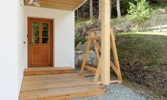 An inviting entrance area with a wooden porch and a beautiful wooden door. The area is surrounded by a green, natural environment.