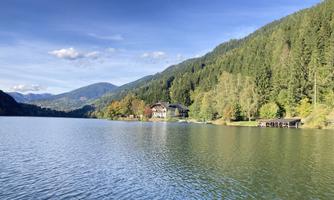 A tranquil lake surrounded by green mountains and colorful foliage. In the background, a charming house can be seen.