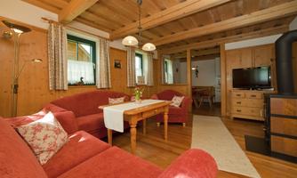 A cozy living room with red sofas and a wooden table. The walls are made of wood, and there is a television as well as a warm, inviting atmosphere.