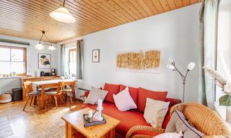 A cozy living room with a red sofa and a wooden table. The walls are light blue and the floor is made of wood.