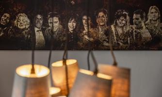 A mural featuring famous musicians and actors in sepia tone style. In the foreground, modern lamps are visible.