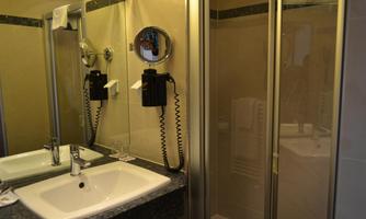 A modern bathroom with a sink and a towel holder. The shower is separated by a glass door.
