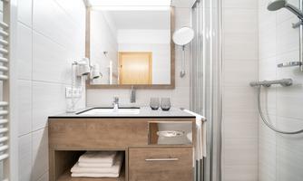 A modern bathroom with a shower and a large mirror. The wooden vanity offers towels and matching accessories.