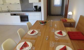 A modern kitchen with a large dining table. The table is set for a meal and there are fresh groceries in a bowl.