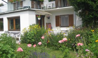 A beautiful house with a balcony and colorful flower pots. The garden is lush with colorful flowers and a cozy seating area.