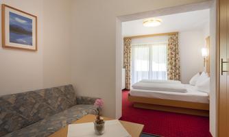 A cozy hotel room with a sleeping area and a seating area. Large windows provide plenty of daylight.