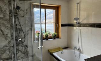 A modern bathroom with a shower and a bathtub. Large windows offer a view of the landscape and plants give the room a cozy atmosphere.
