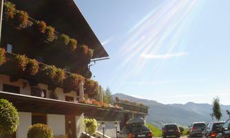A cozy building with beautiful flower balconies. In the background, the mountains stretch out under a clear sky.