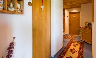 An inviting hallway with a colorful carpet and wooden ceiling. Doors lead to different rooms, while flowers add a touch of color.