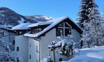 A beautiful house in the snow, surrounded by snow-covered trees. In the background, snowy mountains and a clear blue sky can be seen.