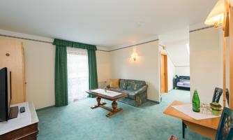 A bright room with green carpet and curtains. There is a couch, a table, and a television.