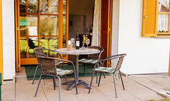 A cozy outdoor area with a round table and four chairs. Drinks and flowers are on the table, surrounded by a sunny atmosphere.
