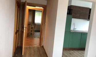 A bright hallway with an open door leading to another room. On the side is a modern kitchen with green cabinets.