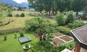 A beautiful garden with various plants and a vegetable garden. In the background, there are trees and a meadow.