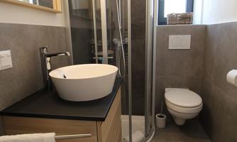 A modern bathroom with a shower and a sink. The walls are painted in neutral colors and there is a large mirror surface.