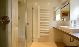 A modern bathroom with a shower and a large mirror. The walls are brightly tiled, and a wooden shelf provides additional storage space.