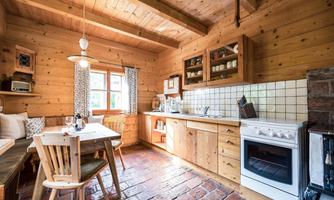 A cozy wooden kitchen with a table and chairs. The windows let in plenty of light and the decor is rustic.