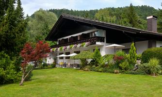 A beautiful house surrounded by a well-maintained garden. The terrace is decorated with sun loungers and plants.
