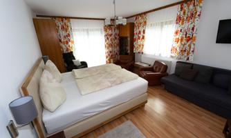 A cozy bedroom with a large bed and colorful curtains. The wooden floors and bright light give the room an inviting atmosphere.