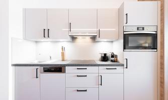 A modern kitchen with white cabinets and a gray countertop. The kitchen appliances are designed in an elegant, minimalist style.