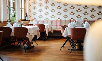 A cozy restaurant with stylish tables and chairs. The walls are decorated with a floral pattern, and the wooden parquet creates a warm atmosphere.