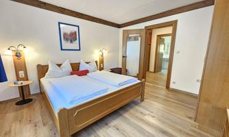 A cozy hotel room with a large bed and two nightstands. The room has a light wooden floor and a warm atmosphere.