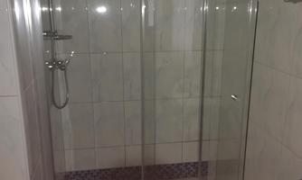 A modern shower with clear glass doors. The walls are designed with bright tiles.