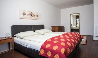 A modern bedroom with a large double bed and red accents. A mirror and a wooden chest of drawers complete the decor.